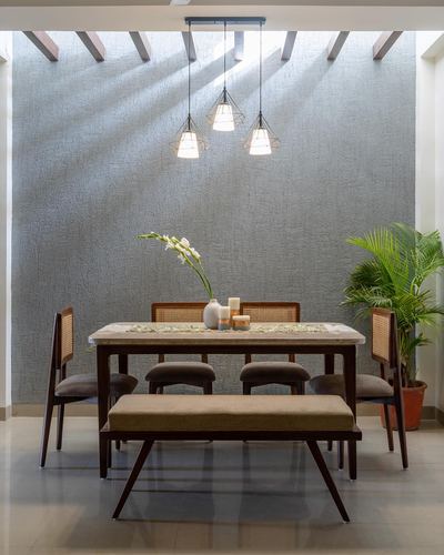 Dining table with cane chairs under geometric pendant lights and striped ceiling shadows