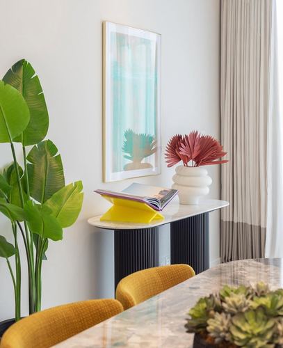 Marble console with art, dried palm arrangement and plants beside mustard velvet dining chairs