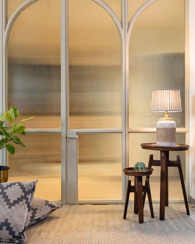 Arched fluted glass doors glow behind a wooden side table with lamp and small stool