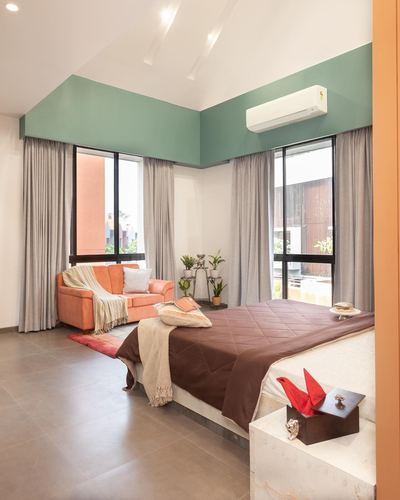 Bedroom with sage green wall, twin windows, orange sofa and brown-quilted bed