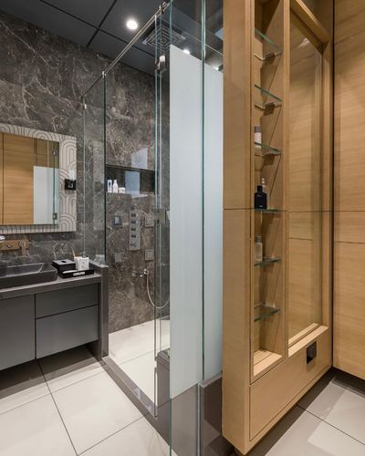 Modern bathroom with marble shower, glass enclosure, and wood shelving column with toiletries