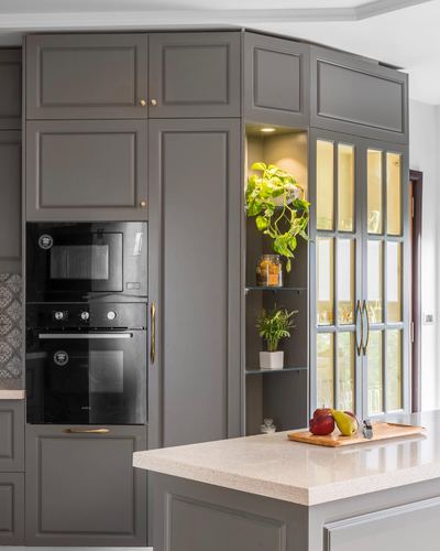 Grey paneled kitchen cabinetry with built-in black oven and glass corner shelves holding plants