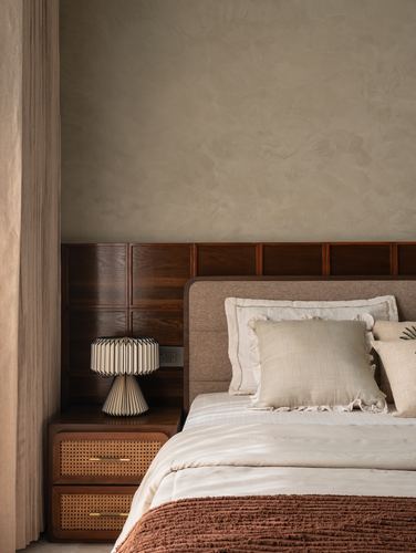 Bedroom corner with fabric headboard, cane nightstand, pleated lamp and terracotta throw