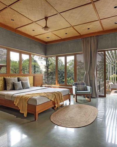 Bedroom with woven cane ceiling grid, wraparound windows to greenery, and mustard-toned bed linen