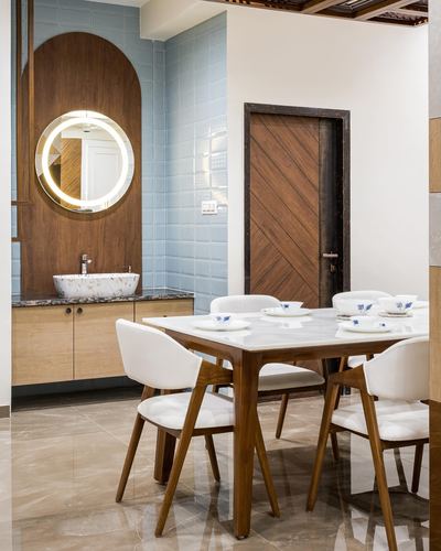 Dining table with white chairs beside an arched wood-framed mirror and washbasin counter