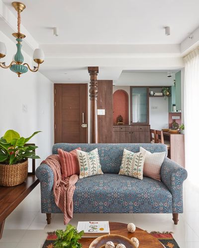 Living room with blue block-print sofa, wooden carved pillar, and arched pooja niche behind