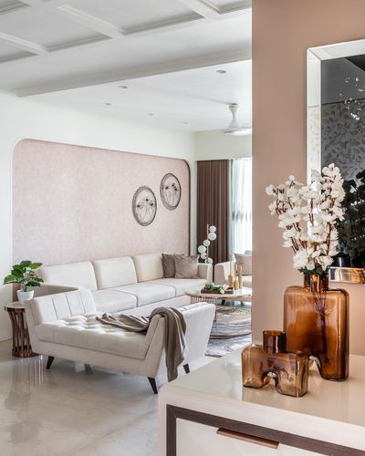 Living room with curved blush wall, cream sofas, marble floor and amber glass vases in foreground