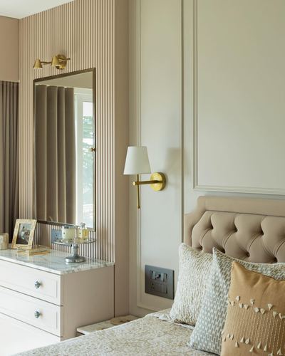 Beige tufted headboard bedroom corner with fluted wall, mirror, and brass sconces