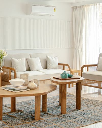 Living room with rattan armchairs, layered round wood coffee tables, and fluted panelled wall