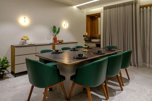 Dining room with dark stone table, green velvet chairs, fluted sideboard, and layered curtains