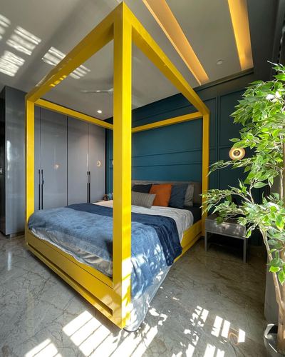 Bedroom with bright yellow four-poster bed frame against teal panelled wall and marble floor
