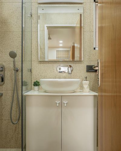 Beige terrazzo bathroom with vessel sink, mirror cabinet reflecting an adjoining room, and glass shower.