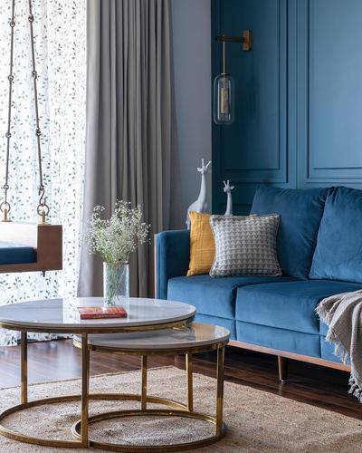 Blue velvet sofa beside a wooden swing and round brass-framed marble coffee tables