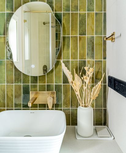 Bathroom with green glazed tile wall, organic mirror, brass fittings and white vessel sink