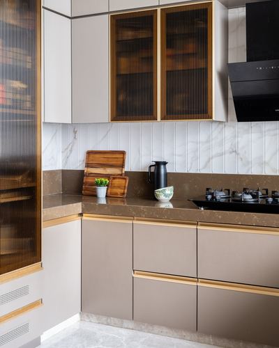 L-shaped kitchen corner with brass-trimmed fluted glass cabinets, marble backsplash and stone counter