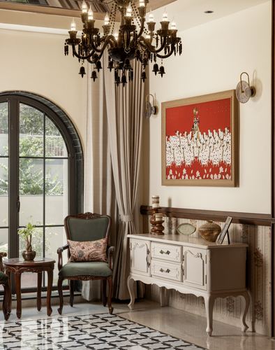 Neo-classical living room corner with arched door, black chandelier, and painted sideboard beneath red artwork