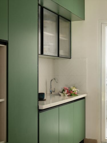 Sage green kitchen cabinetry with herringbone tile backsplash, sink, and fresh flowers on counter