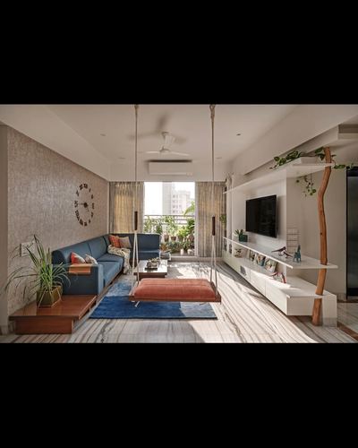 Living room with two hanging swings, blue sofa, orange ottoman, and white shelving unit lit by balcony light