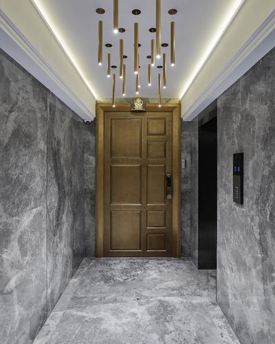Grey stone foyer leading to an ornate brass paneled door beneath a tubular gold pendant light