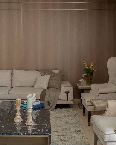 Living room with wood-panelled wall, brass inlay lines, beige sofa, wingback chairs and marble coffee table