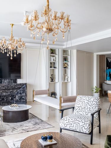 Living room with layered crystal chandeliers, blush swing bench and patterned armchair on marble floor