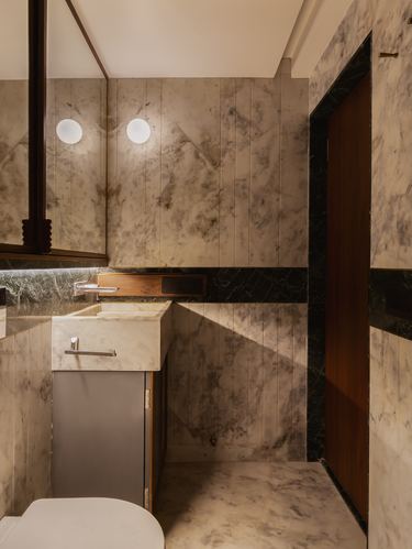 Marble-clad bathroom corner with round sconces, floating sink, and dark wood door