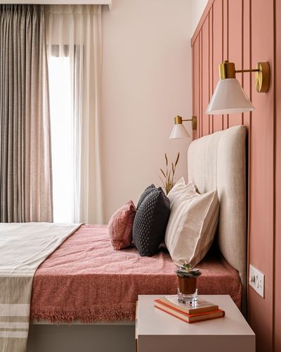 Bedroom corner with terracotta wall panelling, cream headboard, brass sconces and pink throw blanket