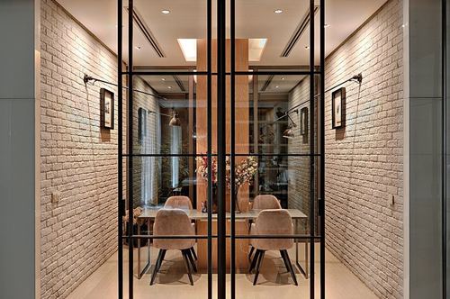 Dining room seen through black-framed glass partition flanked by exposed brick walls