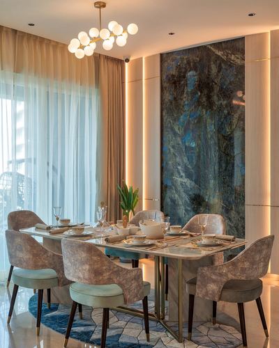 Formal dining room with marble table, cane-back chairs, chandelier, and backlit stone feature wall