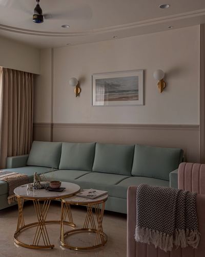 Sage green sofa beneath framed art and brass sconces, gold nesting tables in foreground