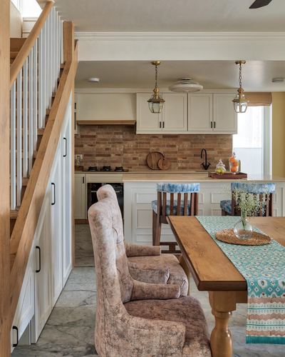 Farmhouse kitchen with brick backsplash, wooden staircase, dining table with velvet chairs in foreground