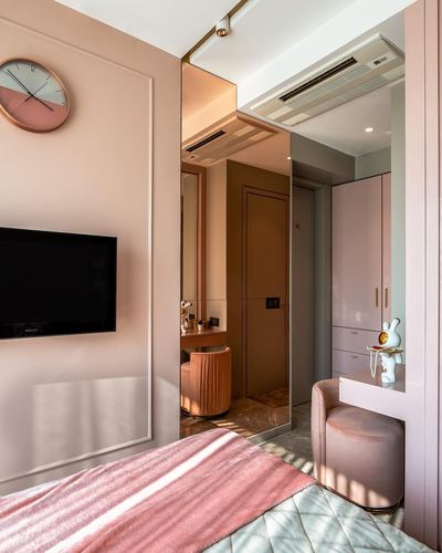 Pink art deco bedroom with mirrored wall, round clock, wall tv and velvet vanity stool