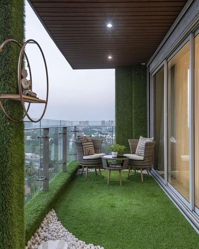 High-rise balcony lined with artificial turf, rattan chairs, and a round wall shelf overlooking a city skyline at dusk