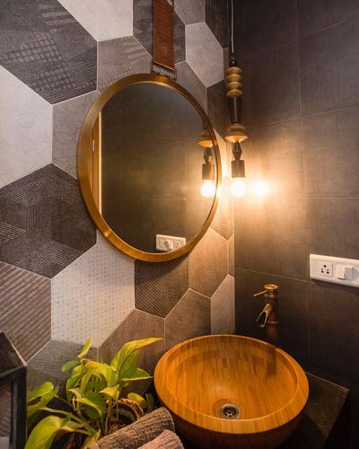 Bathroom vanity with wooden vessel sink, brass faucet, round mirror and pendant bulbs against hexagonal tile wall
