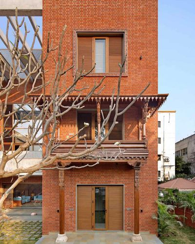 Three-level exposed brick facade with carved wood balcony and louvered shutters, tree branches in foreground