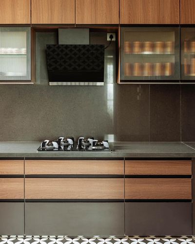 Close-up of modern kitchen with wood cabinetry, dark stone backsplash, chimney hood, and cooktop