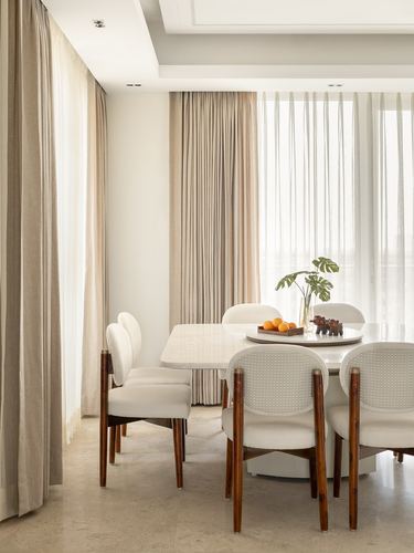 Dining table with cane-back chairs beneath layered curtains and soft daylight