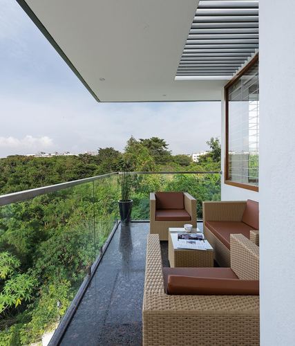 Balcony seating with wicker sofas overlooking a tree canopy in Bangalore