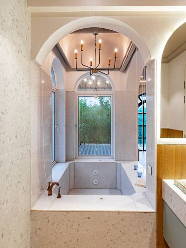Sunken marble bathtub inside arched alcove with chandelier and garden-view window