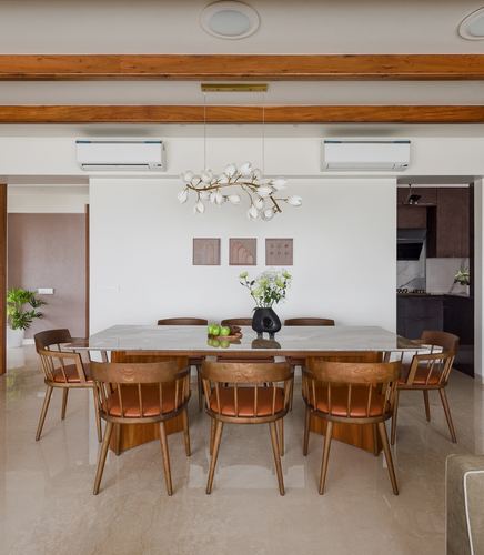 Dining room with marble table, leather-seated wooden chairs, and branch-like pendant light under wood beams