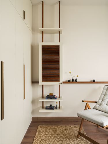 Cream cabinetry corner with a hanging wood-louvered cabinet, floating shelves, and a cane-armed chair on a jute rug