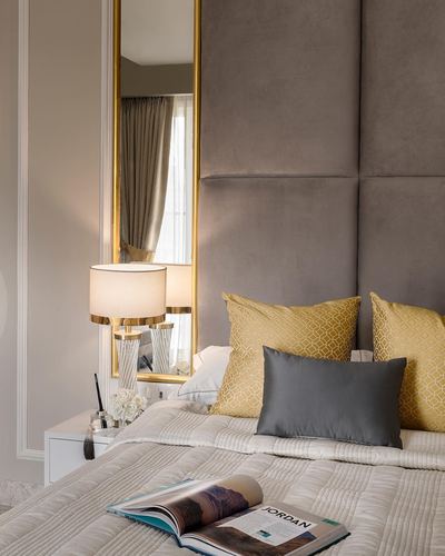 Bedroom corner with grey velvet headboard, gold mirror, brass lamp, and yellow patterned cushions