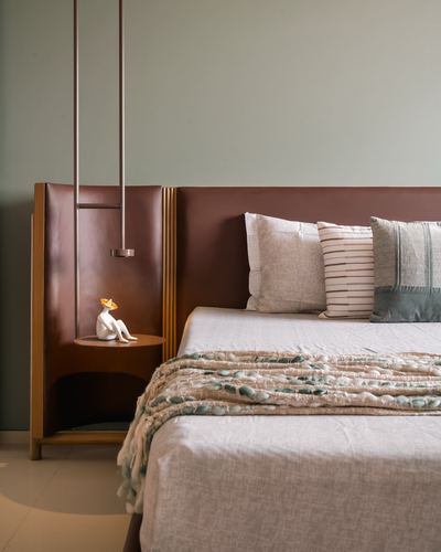 Bedroom with brown leather headboard, curved wooden bedside nook, and layered textured cushions against sage wall