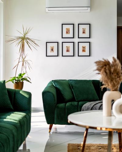 Living room with green velvet sofas, gallery wall, marble table, and indoor plants
