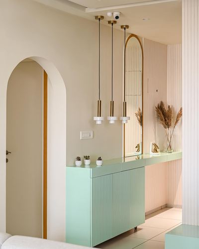 Mint green fluted console with arched brass-trimmed mirror in a pastel foyer with three pendant lights