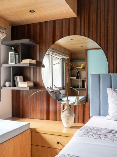 Wood-panelled bedroom with round mirror over nightstand, ceramic vase, and blue upholstered headboard.