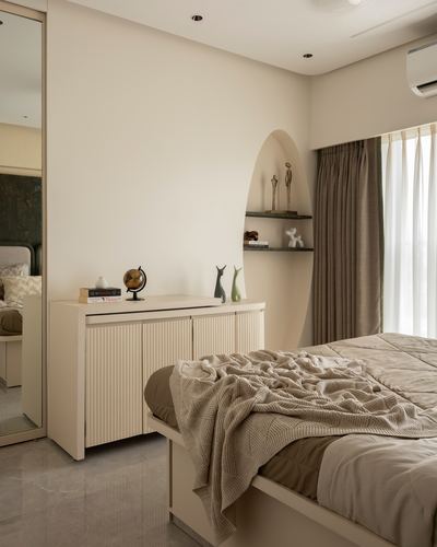 Beige bedroom with fluted sideboard, arched niche shelves, and layered bed linens near sheer curtained window