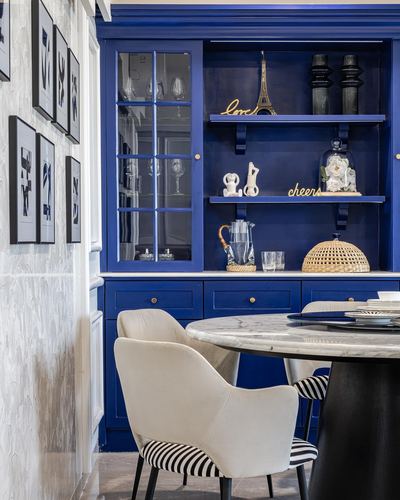 Cobalt blue dining hutch with glass doors beside a round marble table and striped chairs.