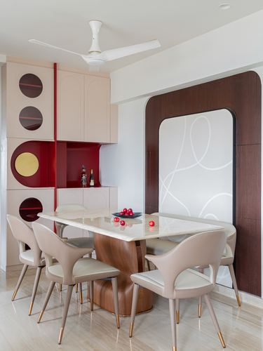Dining room with marble table on sculpted wood base, cream chairs, and maroon circular cabinet accents