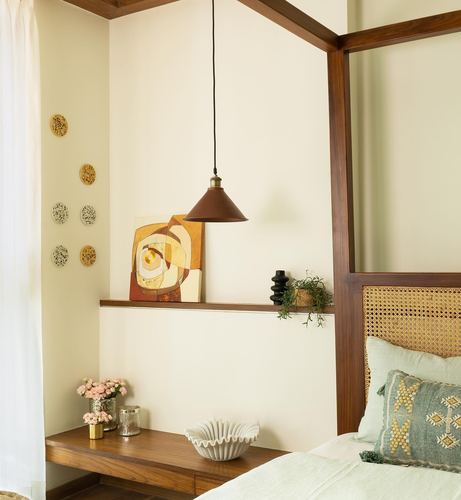 Bedroom corner with cane headboard, wooden four-poster frame, pendant light, and shelf styled with art and ceramics